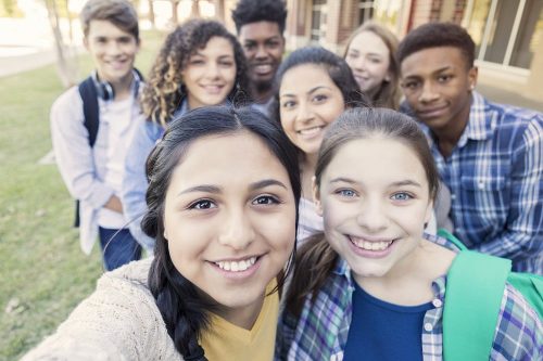 Diverse group of teens looking at camera taking selfie at high school